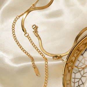 Close-up of golden double-layer ball and snake chain necklace with clasp on beige silk