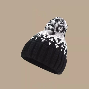 Detail of knitted winter beanie with mixed color pompom and geometric snowflake pattern