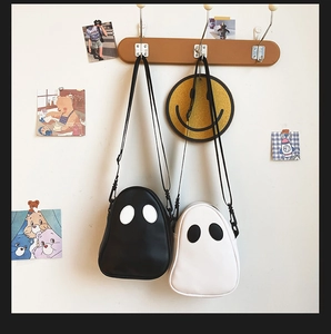 Ghost shaped crossbody bags in black and white PU leather hanging on a wooden hook