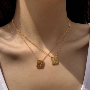 Close-up of model wearing double-layered gold square necklaces with Z and C letter charms