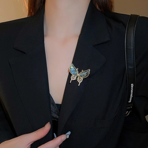 Détail d'une broche papillon dorée avec nacre colorée portée sur un tailleur noir