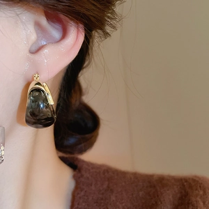 Close-up of U-shaped resin earring with gold metal base on model wearing brown sweater