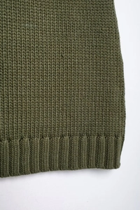 Macro del maglione verde in maglia che mostra l'orlo a coste testurizzato e il tessuto di lana