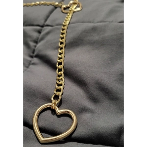 Close-up of golden gothic heart pendant with chunky Cuban chain on dark fabric texture