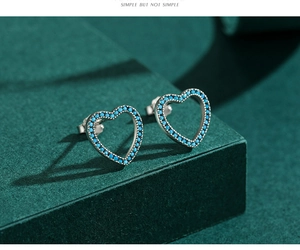 Détail macro de boucles d'oreilles cœur en argent avec turquoise sur fond vert