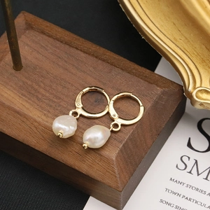 Detail of baroque pearl drop earrings featuring gold-plated metal hoops on a wooden base