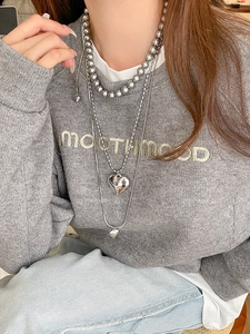Close-up of layered heart pendant necklaces with grey pearls and silver snake chain