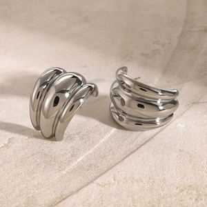 Macro shot of silver chunky triple-layer arched earrings on a textured stone surface