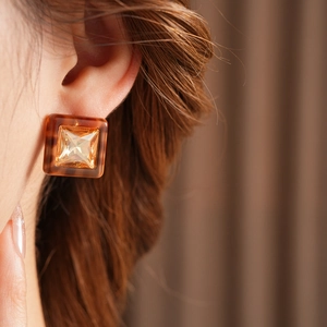 Close-up of square amber resin earrings with a gold faceted center stone on a model