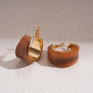 Close-up of C-shaped resin hoop earrings in amber brown with gold metal lining