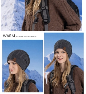 Close-up of cable knit beanie with leather logo patch against a snowy outdoor background