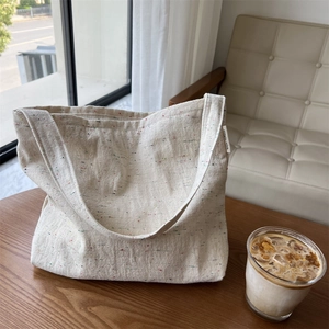 Dettaglio di una borsa tote in tela crema con fibre colorate su un tavolo di legno