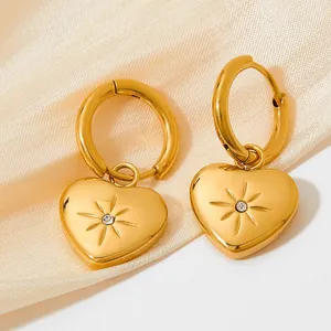 Close-up of gold heart earrings with starburst engraving on a beige silk background