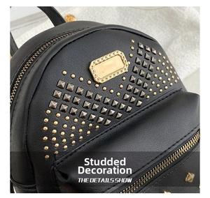 Macro detail of black pebble leather backpack featuring gold pyramid studs and metal plaque