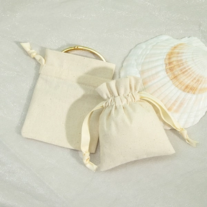 Detail of beige cotton linen jewelry pouches shown flat and cinched on a seashell set
