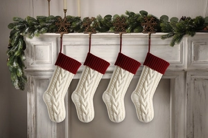 Four white cable knit Christmas stockings with red cuffs hanging on a festive mantelpiece