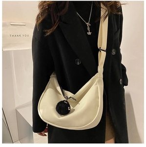 Close-up of beige half-moon crossbody bag with wide strap and fuzzy charm on model