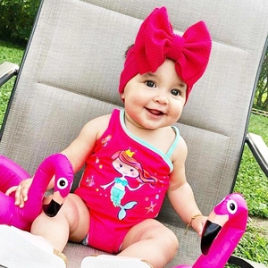 Detail of bright pink baby girl swimsuit featuring mermaid print and bow headband