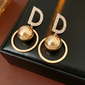 Detail of golden D-letter earrings with crystals, metal sphere and large ring