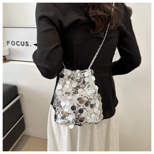 Macro detail of silver sequin bucket bag with shimmering metallic chain strap on shoulder