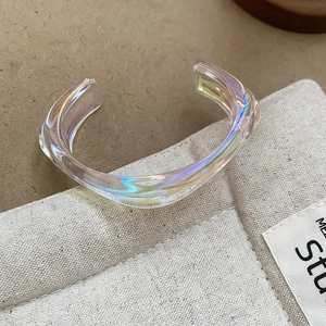 Macro shot of iridescent wavy acrylic bangle showing colorful aurora light effects on fabric