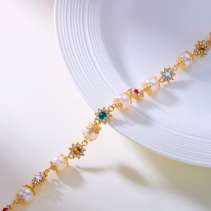 Elegant gold bracelet with pearls and colorful gemstone flowers on a white dish