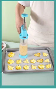 Manual cookie press gun set with clear tube making various biscuit shapes on a baking tray