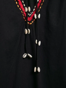Détail de la broderie ethnique et des glands en coquillages sur une robe noire