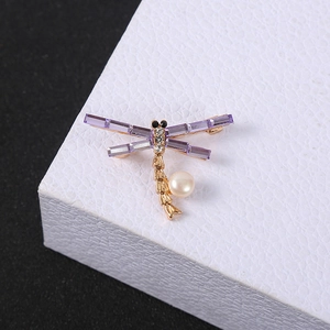 Golden dragonfly brooch with purple crystal wings and a white pearl on white stand