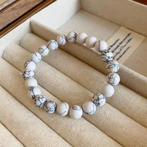 Détail d'un bracelet en perles de marbre blanc veiné de noir dans un écrin beige