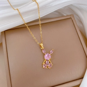 Close-up of pink crystal rabbit pendant on gold-plated chain over silk background