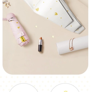 Flat lay of a mini pink and white 5-fold sun umbrella with gold hearts and UPF50+ label