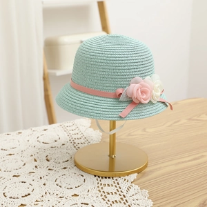 Detail of mint green straw hat with pink ribbon and fabric flowers on gold stand