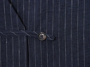Macro detail of navy pinstripe linen fabric with a single black button and buckle closure