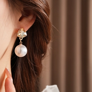 Detail of luxury triangle gemstone and white pearl dangle earrings worn by a model