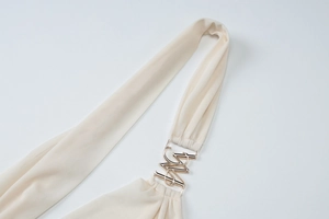 Detail view of a gold metallic buckle on a creamy white mesh top shoulder strap