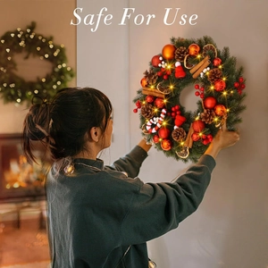 Christmas wreath with LED lights pine cones and ornaments hanging on a white wall
