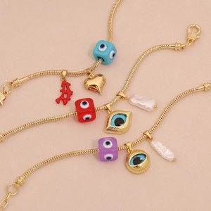 Detail of three gold snake chain bracelets featuring evil eye charms and baroque pearls