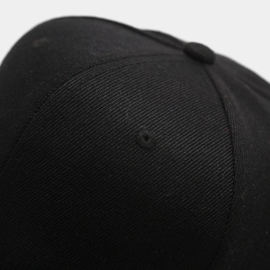 Close-up of a black hip hop cap showing cotton twill fabric texture and embroidered eyelet