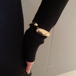 Polished gold drop open cuff bracelet styled over a black knit sleeve for women