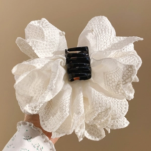 Close-up of white lace bow hair claw clip with intricate fabric textures and black base