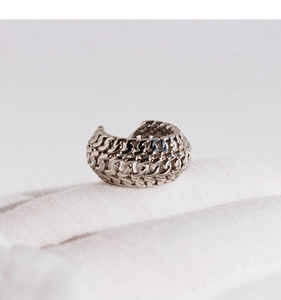 Close-up of silver hollow triple-row chain ear cuff on white textured fabric background
