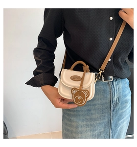 Close-up of a white mini square crossbody bag with a brown bear charm on a model