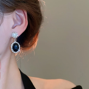 Macro shot of black oval zircon drop earrings with flower stud detail on a female model