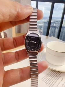 Close-up of a silver metal strap and oval black dial watch held against a city view