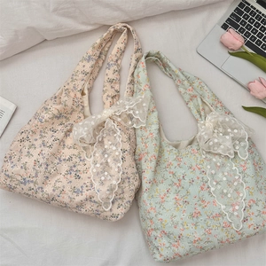 Detailed shot of beige and green floral canvas tote bags with white lace bow accents