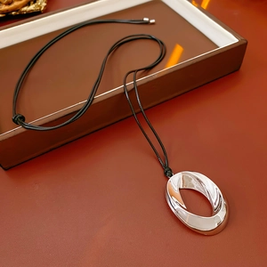 Silver oval metal pendant on a thin black cord necklace over brown leather texture