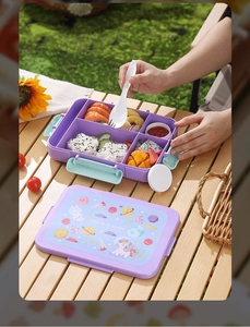 Detail of purple multi-compartment bento box with a space-themed lid and a white spoon