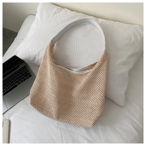 Flat lay of a beige woven mesh shoulder bag with white straps on a bed setting