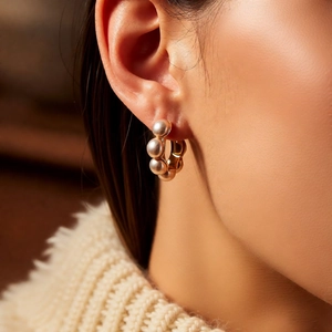 Gros plan de boucles d'oreilles créoles dorées avec perles portées sur un pull